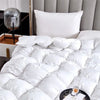 A close-up of a white goose down quilt with numerous fluffy white pillows on a bed.