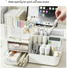A white desk organizer with transparent drawers holds various stationery and office supplies.