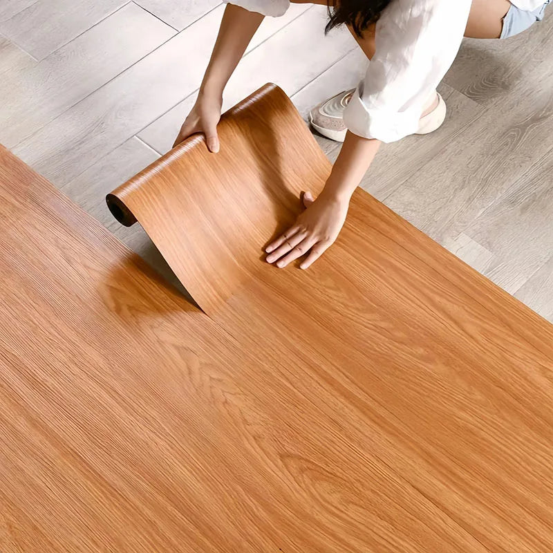 A person is applying self-adhesive wood grain wallpaper to a wooden surface.