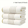 Three white bath towels with gold stripes stacked together.