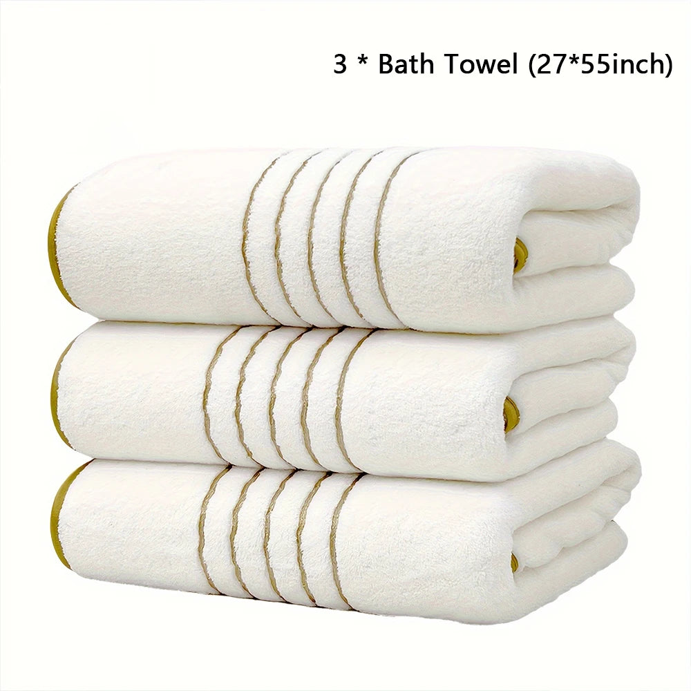 Three white bath towels with gold stripes stacked together.