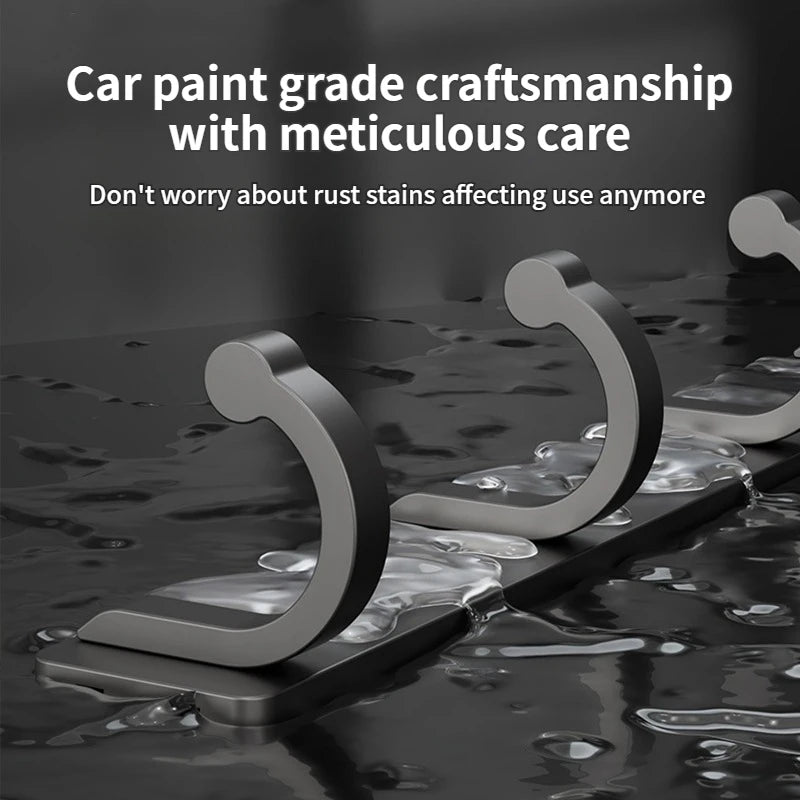 A set of six gray no-drill aluminum wall hooks with adhesive backing are shown resting on a dark, wet surface.
