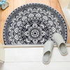 A black and white tribal boho semi-circle doormat is displayed next to a pair of light gray woven slippers.