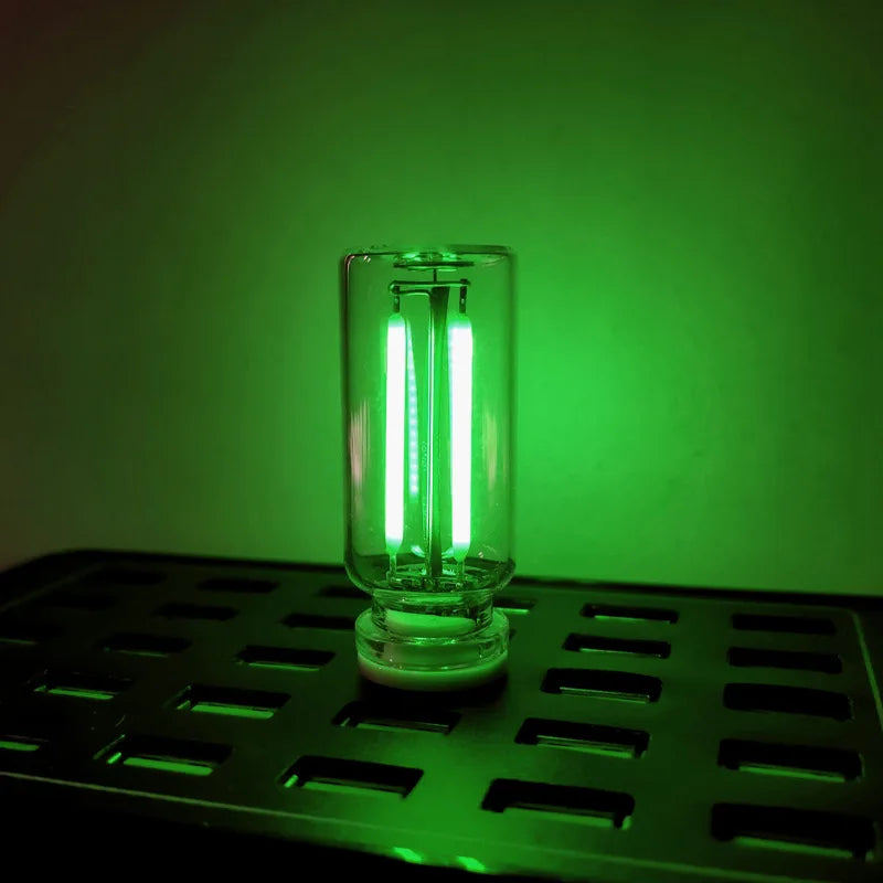 A clear glass LED night light with a warm filament glow is illuminated against a green background.