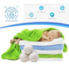 A newborn baby is sleeping on a white towel surrounded by natural wool dryer balls and green fabric.