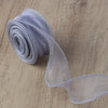 A roll of sheer, silvery-gray organza ribbon unwinding on a wooden surface.