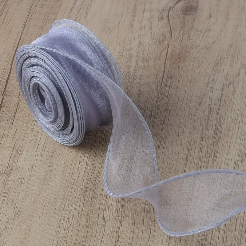 A roll of sheer, silvery-gray organza ribbon unwinding on a wooden surface.