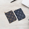 A dark gray patterned compact zippered card holder wallet placed on a light wooden surface next to a pen and a white notebook