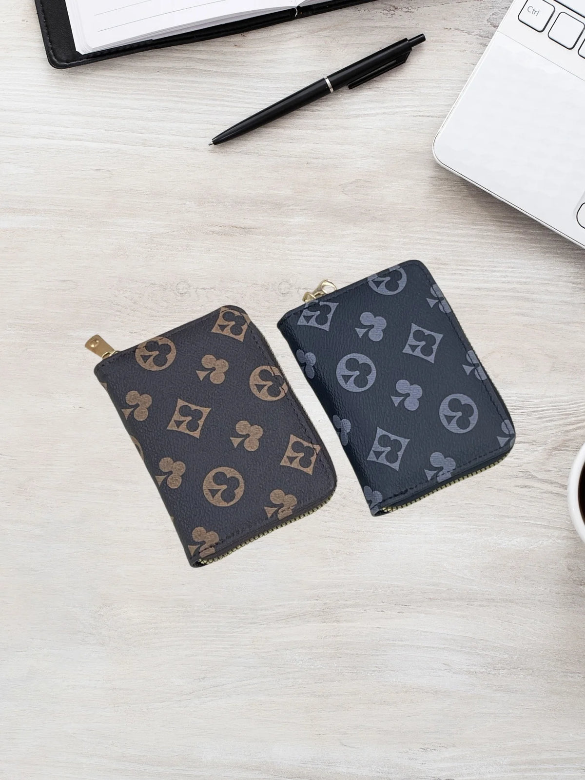 A dark gray patterned compact zippered card holder wallet placed on a light wooden surface next to a pen and a white notebook