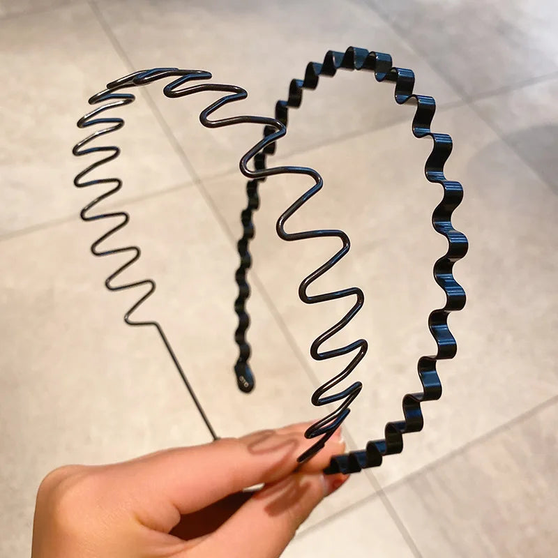Eine Hand hält ein schwarzes, elastisches Metall-Haarband mit gewellten Locken, das seine Flexibilität demonstriert.