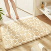 A beige plush non-slip absorbent bathroom rug with a pebble texture placed on a wooden floor.