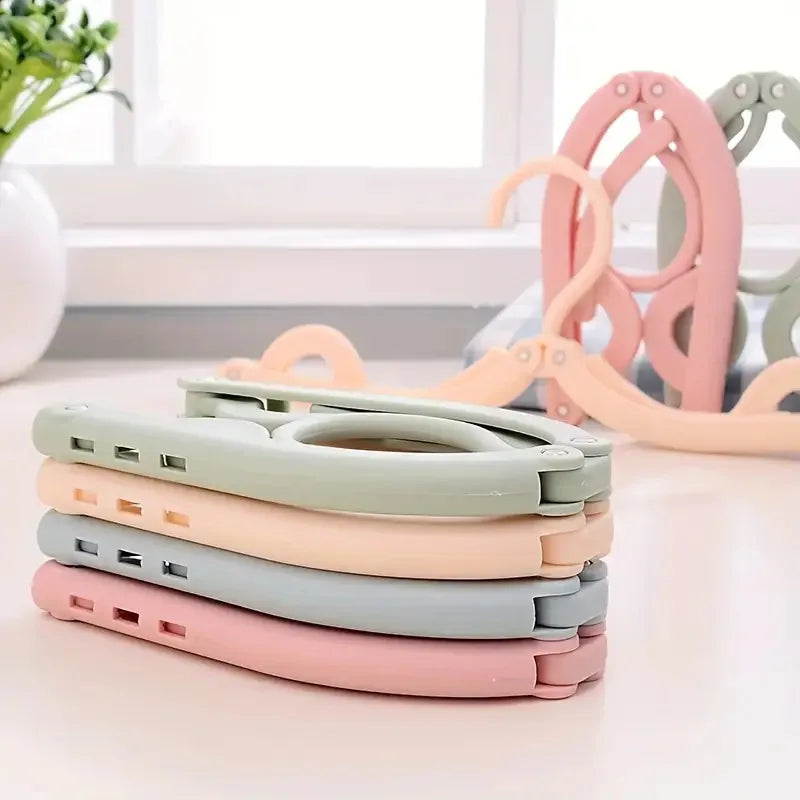 A stack of ten foldable travel clothes hangers in various pastel colors, including pink, beige, and green.