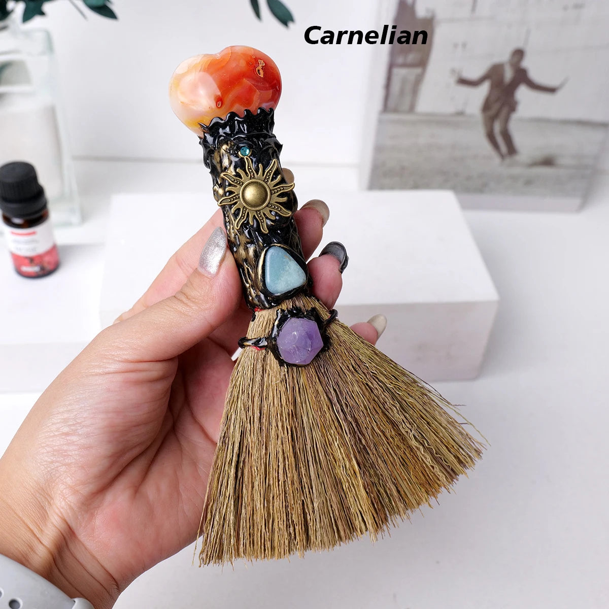 Una mano sostiene una escoba de corazón de cristal natural con varias cristales de colores como naranja, azul y púrpura.