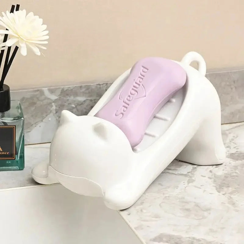 A white cat-shaped soap dish with a purple insert and drainage tray sits on a marble surface.