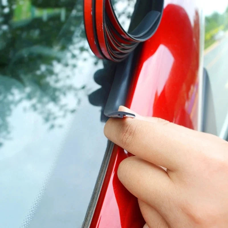 A hand is holding a black rubber sealing strip on a red automotive surface for noise and weather protection.