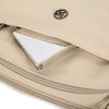 A beige nylon crossbody bag with a silver logo and an open pocket showing a reflective lining.