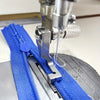 Stainless steel invisible zipper presser foot attached to a sewing machine needle and blue fabric.