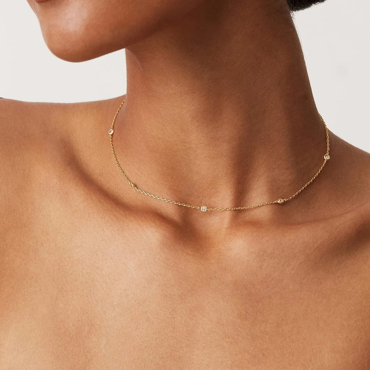 A close-up of a gold-toned necklace with small diamond accents worn around the neck.