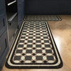 A rectangular kitchen rug with a classic black and beige geometric pattern placed on a light wood floor.