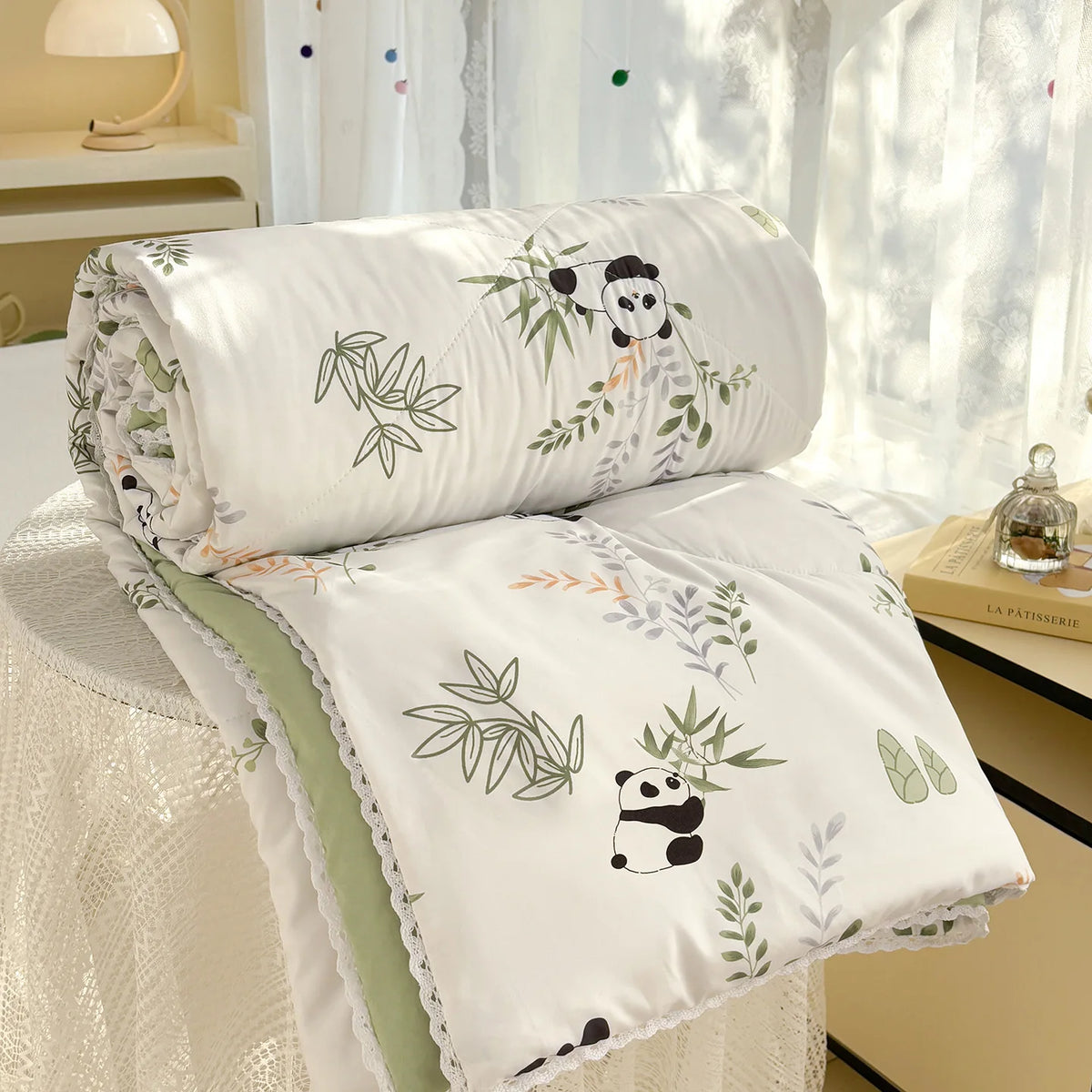 White comforter with a panda print and lace trim resting on a white table near a window.