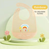 A pink silicone baby bib with a rainbow design and six adjustable buckles is displayed on a light green surface.