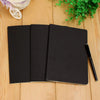 A black A6 kraft paper blank notebook open on a wooden surface with a black pen.