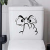 A white toilet lid features a black line drawing of an expressive, angry face.