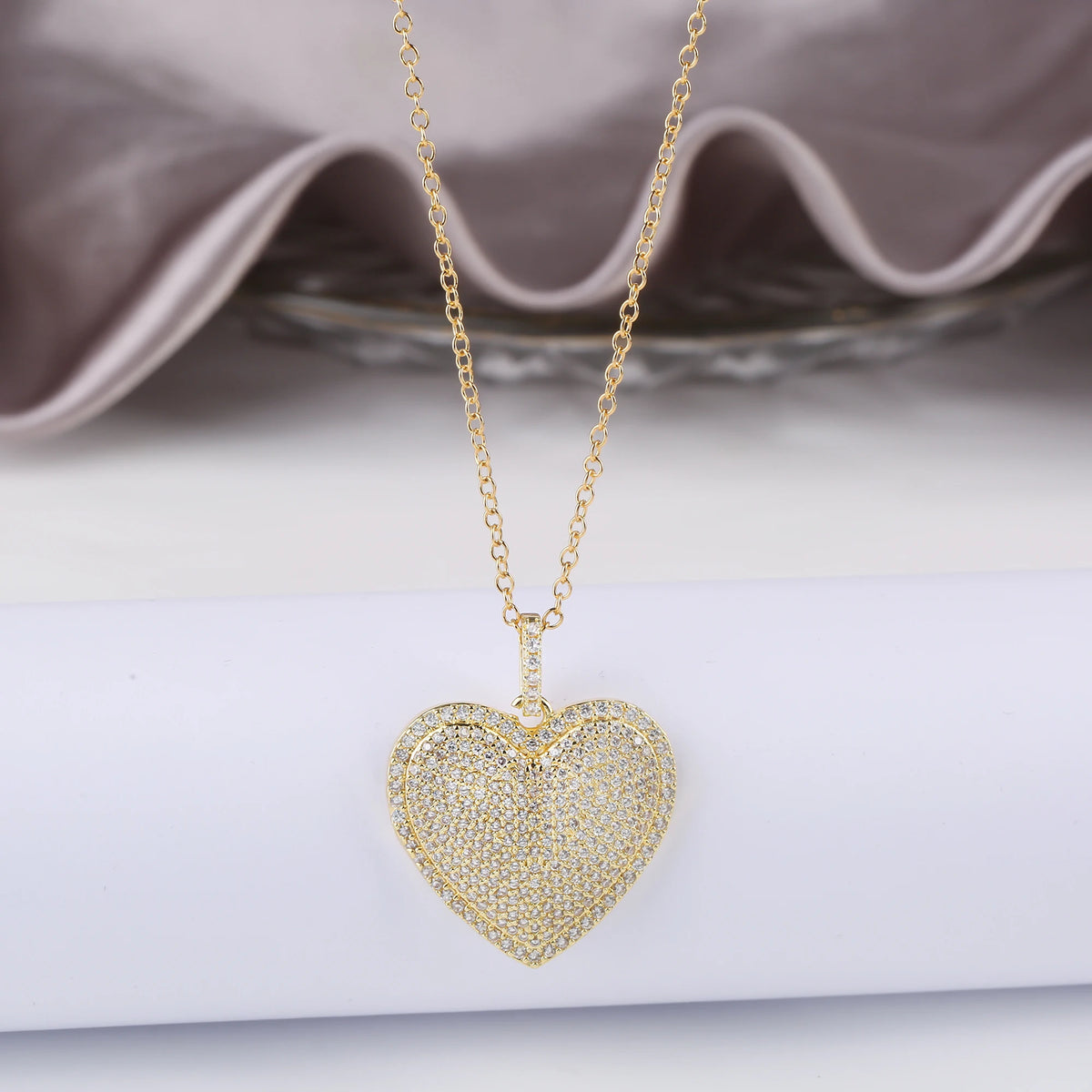 Gold chain necklace with a heart-shaped cubic zirconia pendant resting on a white surface.