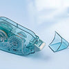 A clear double-sided adhesive tape roller for crafts and office use is shown on a light blue background.