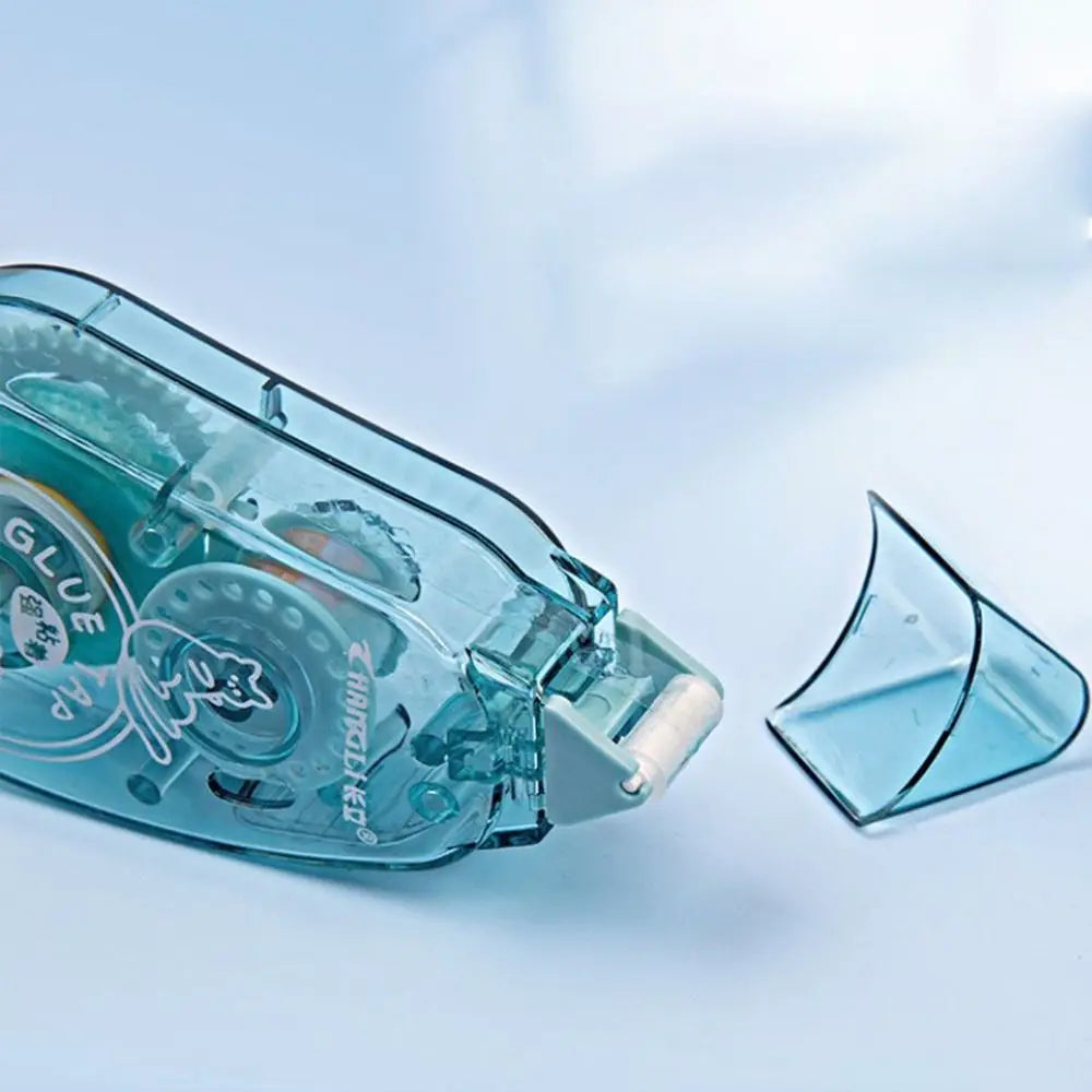 A clear double-sided adhesive tape roller for crafts and office use is shown on a light blue background.