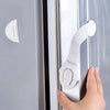 A hand is operating an adhesive baby proofing latch on a cabinet door, demonstrating a child safety lock mechanism.