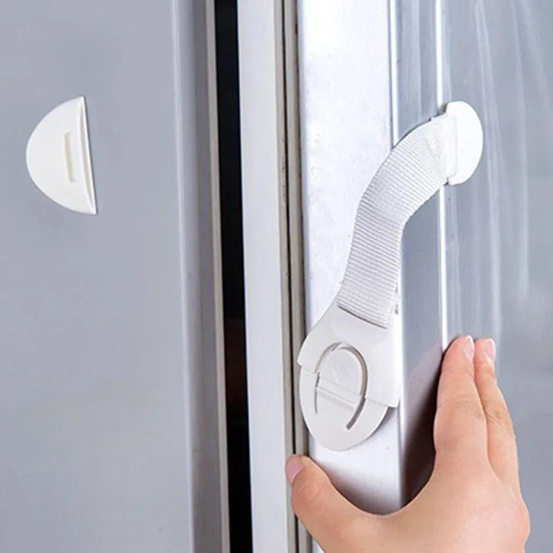 A hand is operating an adhesive baby proofing latch on a cabinet door, demonstrating a child safety lock mechanism.