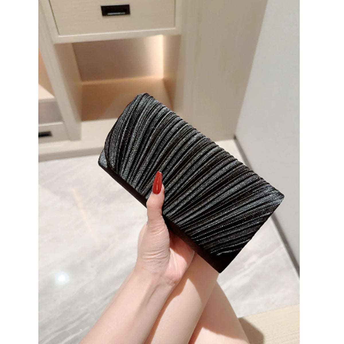 A close-up shot of a black patent leather clutch bag with a textured pattern held by a hand.
