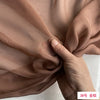 Close-up of a hand folding a piece of light brown sheer silk chiffon fabric.