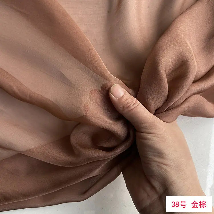 Close-up of a hand folding a piece of light brown sheer silk chiffon fabric.