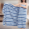 A woman is holding a blue and white striped microfiber bath towel against her body.
