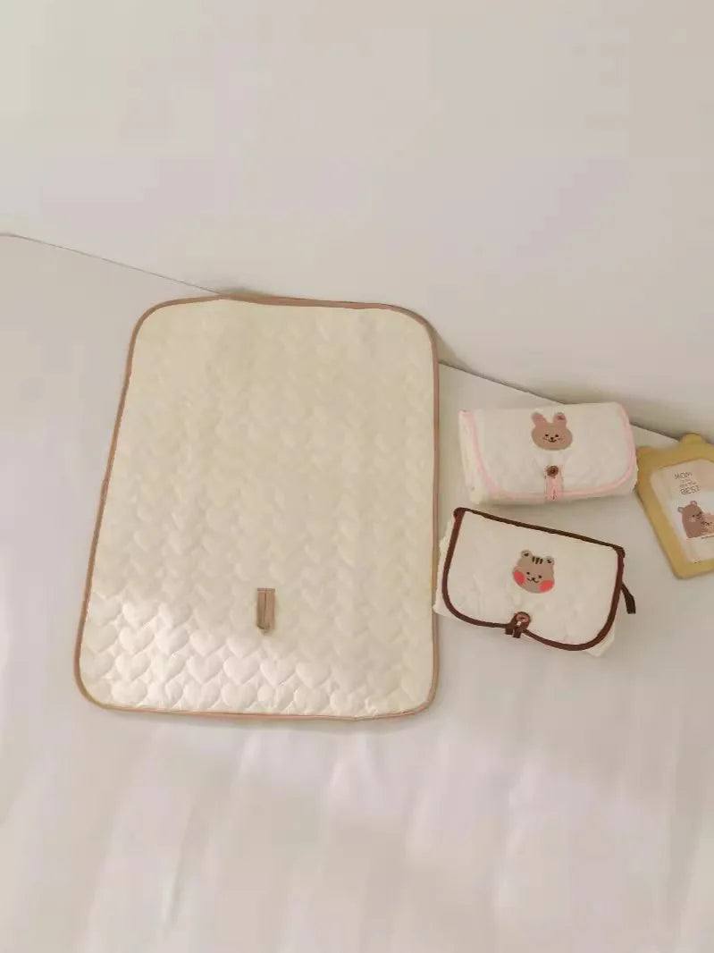 A beige quilted foldable portable diaper changing pad with several small fabric pouches.