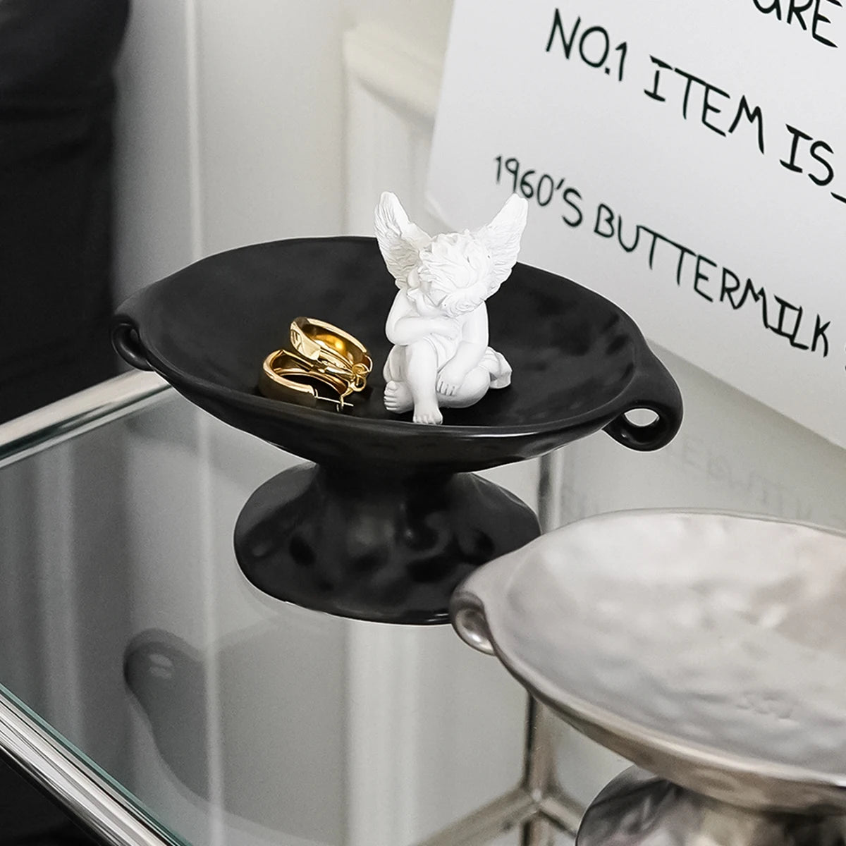 A black ceramic soap dish with an elevated stand holds a white dove figurine and gold rings.