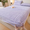 A purple faux fur fitted sheet is draped over a bed, with a hand holding the bottom edge.