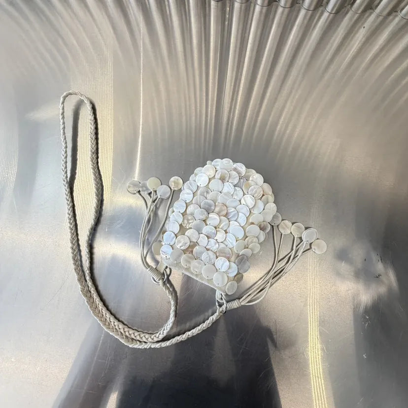 A clear acrylic chain shoulder bag adorned with round white sequins resting on a reflective surface.