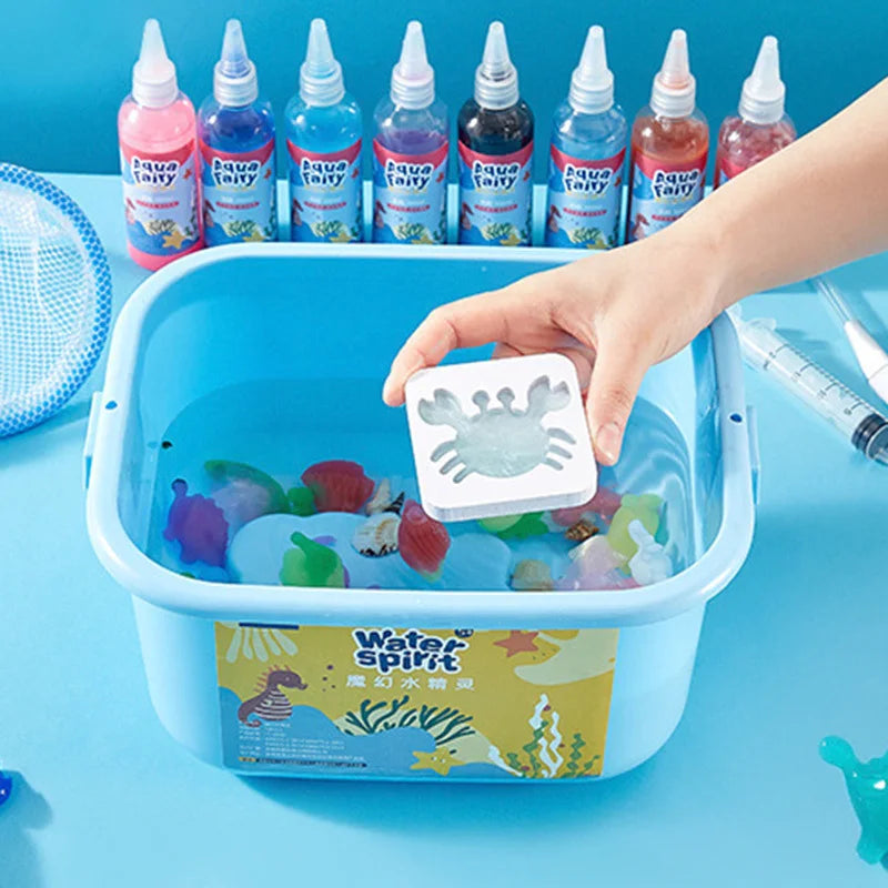 A hand is holding a blue plastic container filled with water and various colored craft items, including bottles of liquid and