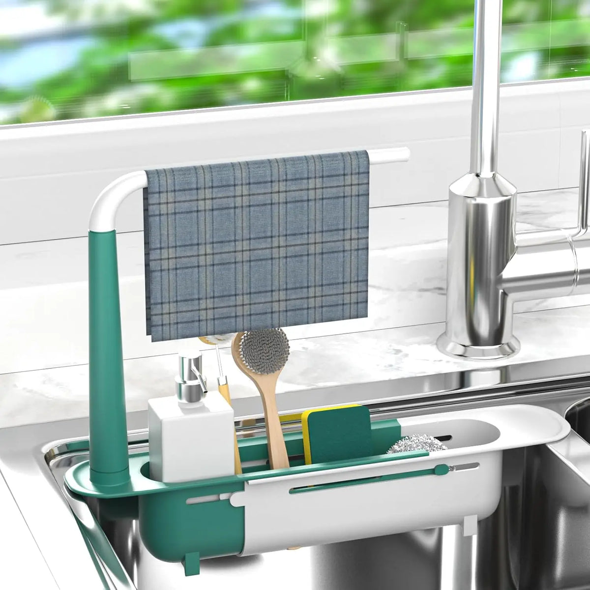 A silver adjustable over-sink dish drying rack with a teal handle and a blue plaid dishcloth is placed in a kitchen sink.
