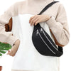 A close-up of a black nylon waist pack with a zipper and adjustable strap worn on a light beige sweater.
