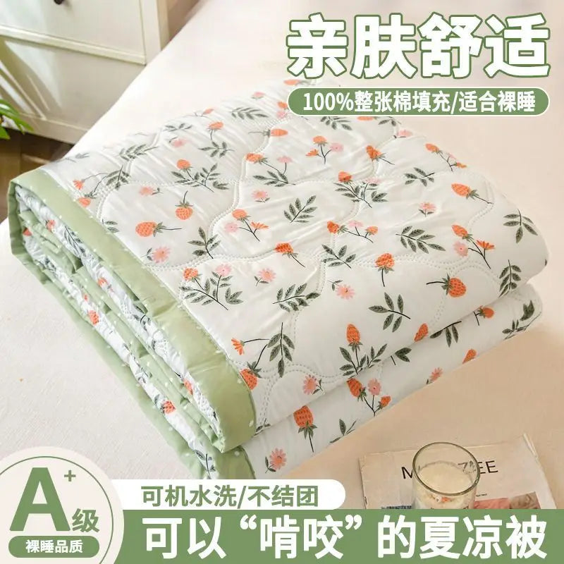 A quilted white blanket with a floral pattern is shown folded on a bed, emphasizing its light and breathable comfort.