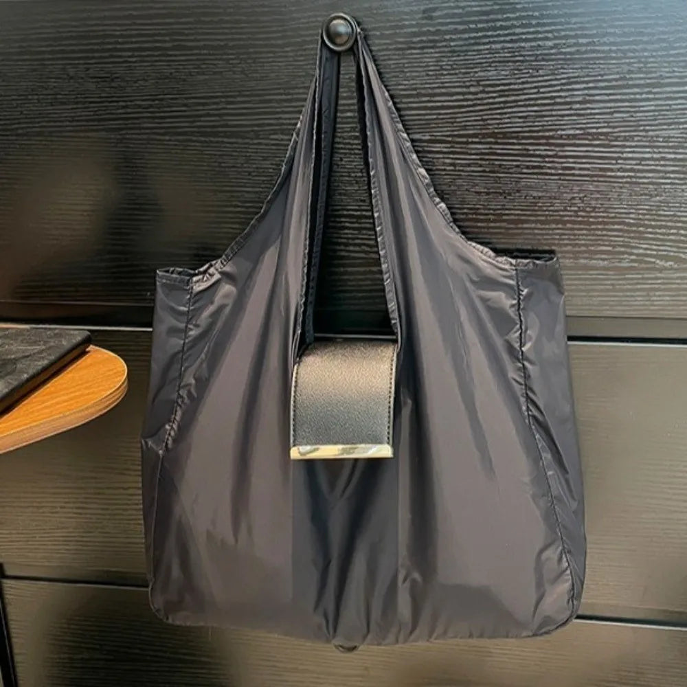 A dark gray retractable keychain tote bag folded into a compact pouch, hanging against a dark wood background.