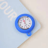 A blue silicone pocket watch with a silver face and pink accent is pinned to a light blue card.