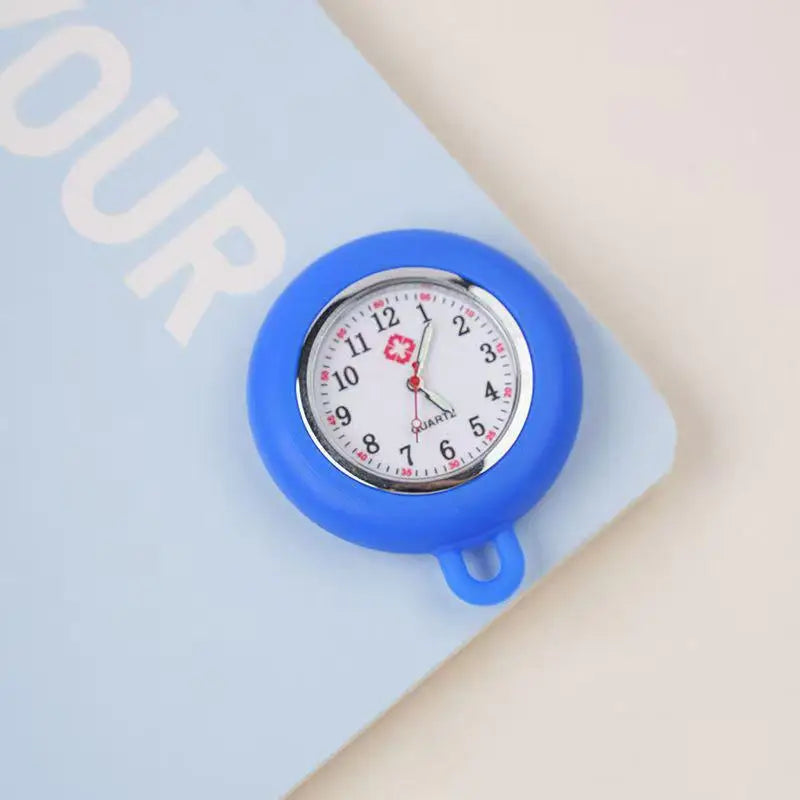 A blue silicone pocket watch with a silver face and pink accent is pinned to a light blue card.