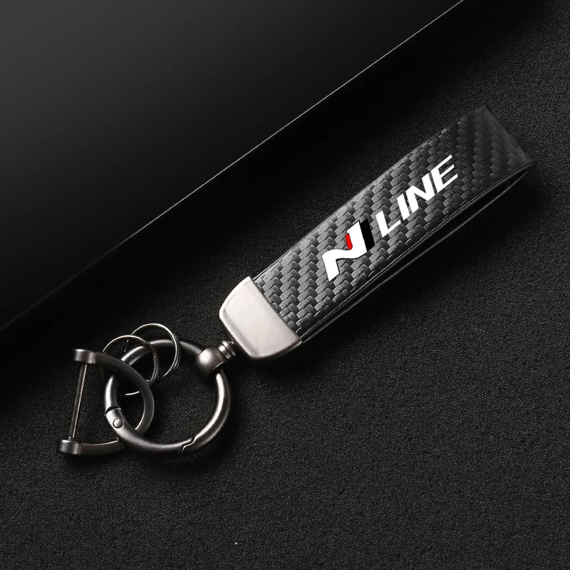 A black carbon fiber style leather keychain with a silver swivel buckle resting on a dark surface.