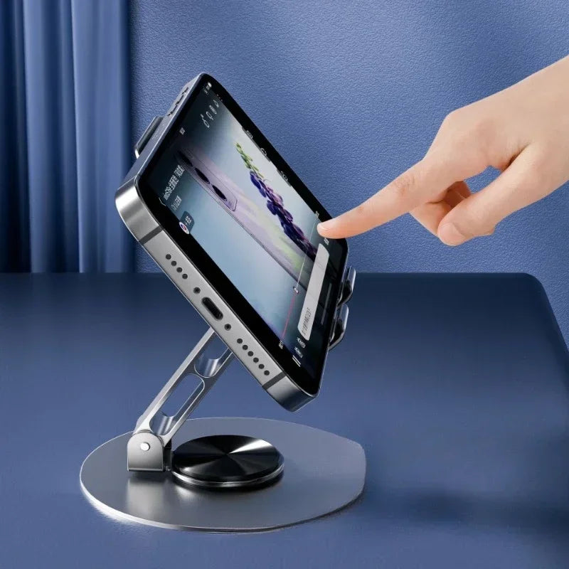 Una mano está rotando un smartphone en un soporte giratorio de 360 grados para escritorio.