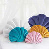 A collection of velvet shell print throw pillows in shades of purple, white, yellow, and teal resting on a white surface.